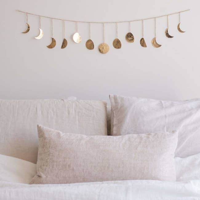 A gold garland strung above a bed with moons in waxing and waning phases strung along it 