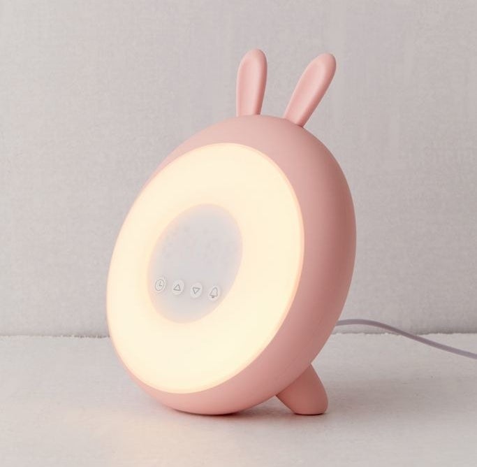 round alarm clock with pink frame and small bunny ears on top and round light and four buttons in the center