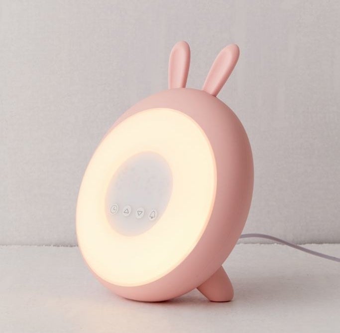 round alarm clock with pink frame and small bunny ears on top and round light and four buttons in the center