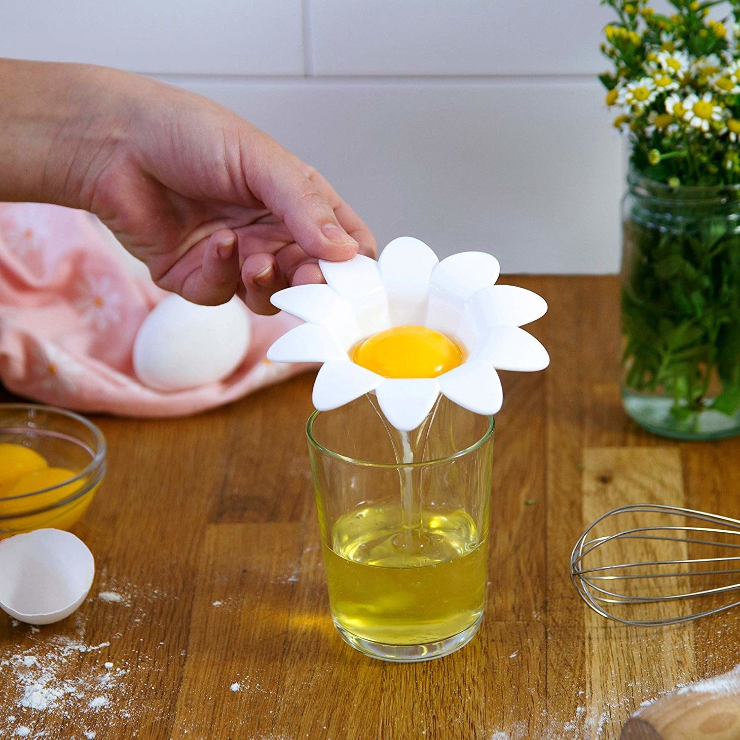 a small cup that looks like a daisy in white with an egg yolk in the middle and the egg whiles pouring into a glass below it