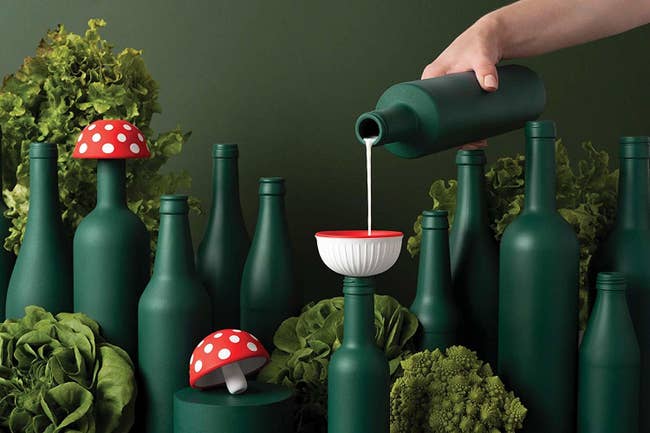 hand pouring a liquid from one bottle to another through the bowl-shaped mushroom funnel