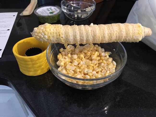 A reviewer's stripped corn cob sitting next to a bowl of corn kernels and the cob stripper