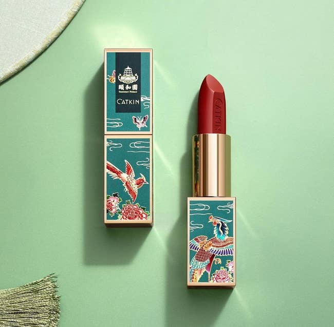 the tube of lipstick in teal with gem-colored illustration of birds on it