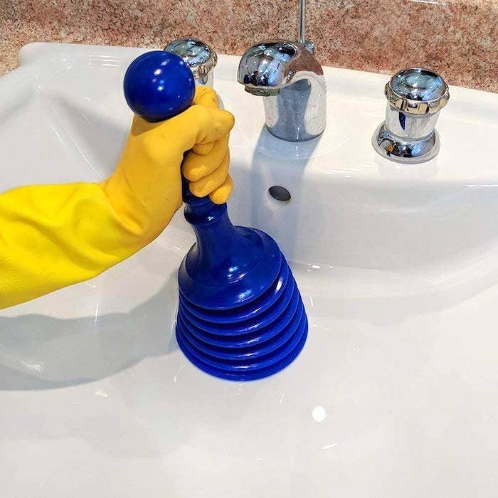 reviewer&#x27;s hand holding a mini plunger inside a sink