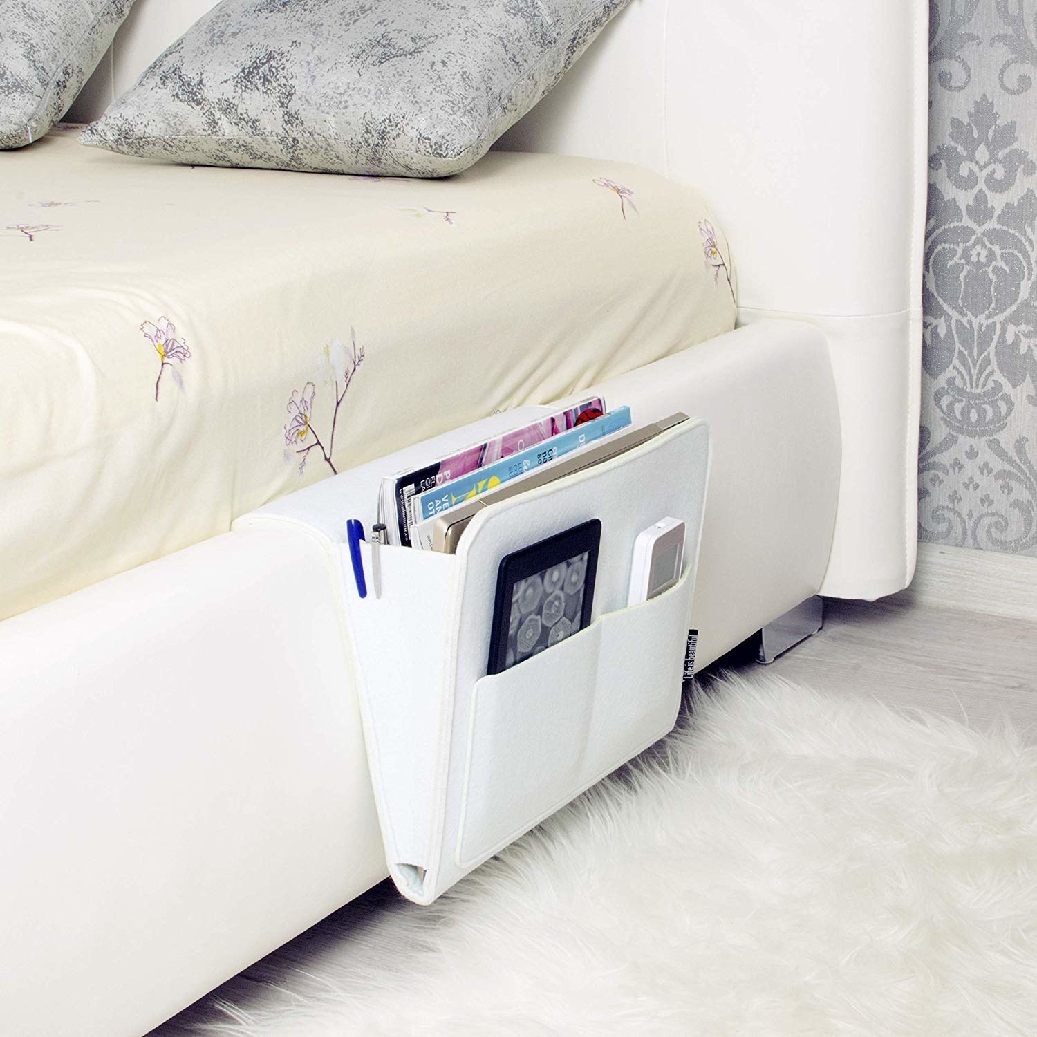 A bedside caddy attached to a bed with magazines, stationery and other items placed in it