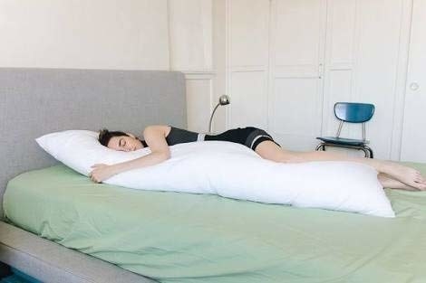 A person on a bed sleeping on their side while hugging the body pillow