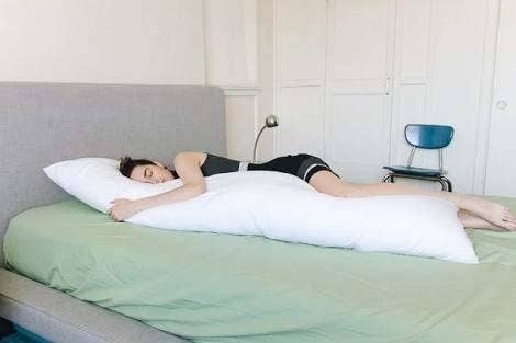 A person sleeping snuggled with the white body pillow.