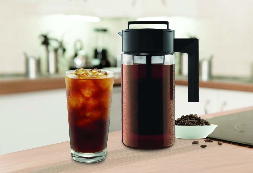 The cold brew coffee pitcher next to a glass of cold brew 