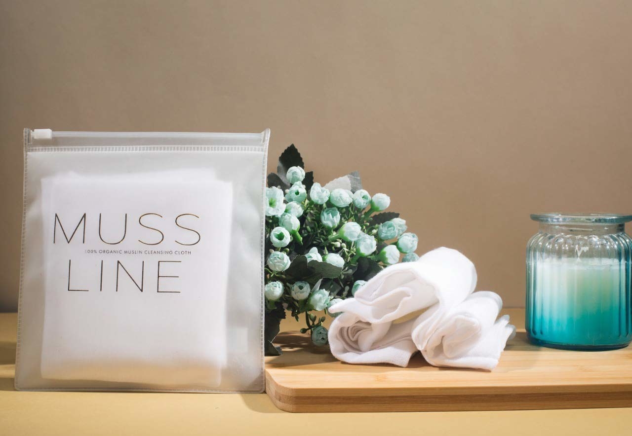 A closed pouch of muslin makeup remover pads on a table next to some used pads