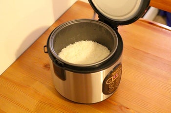 The rice cooker with its lid off to show rice cooking inside 