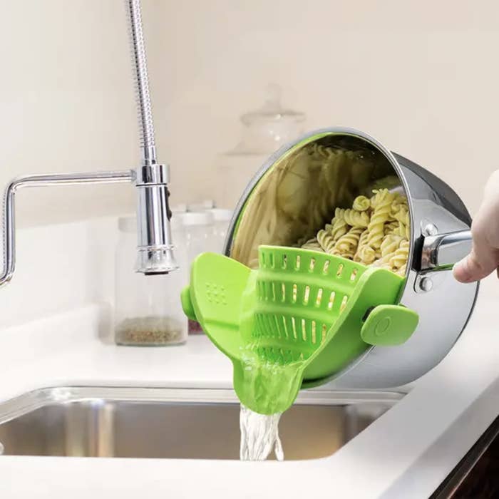 A model straining pasta from a green strainer clipped to the sides of the pot 