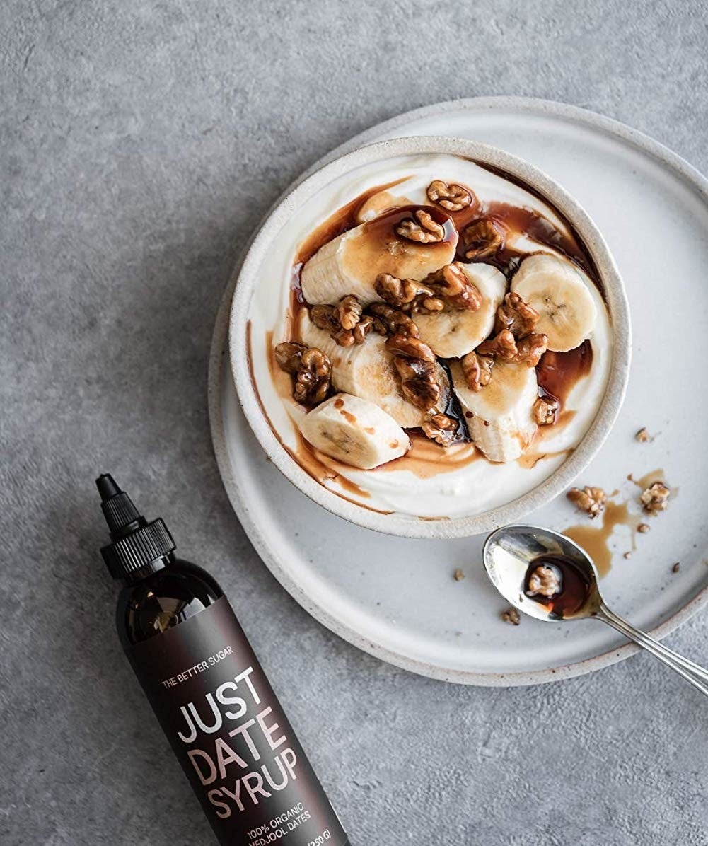 bowl of yogurt and bananas with dark date syrup drizzled on it next to the squeeze bottle that says just date syrup 