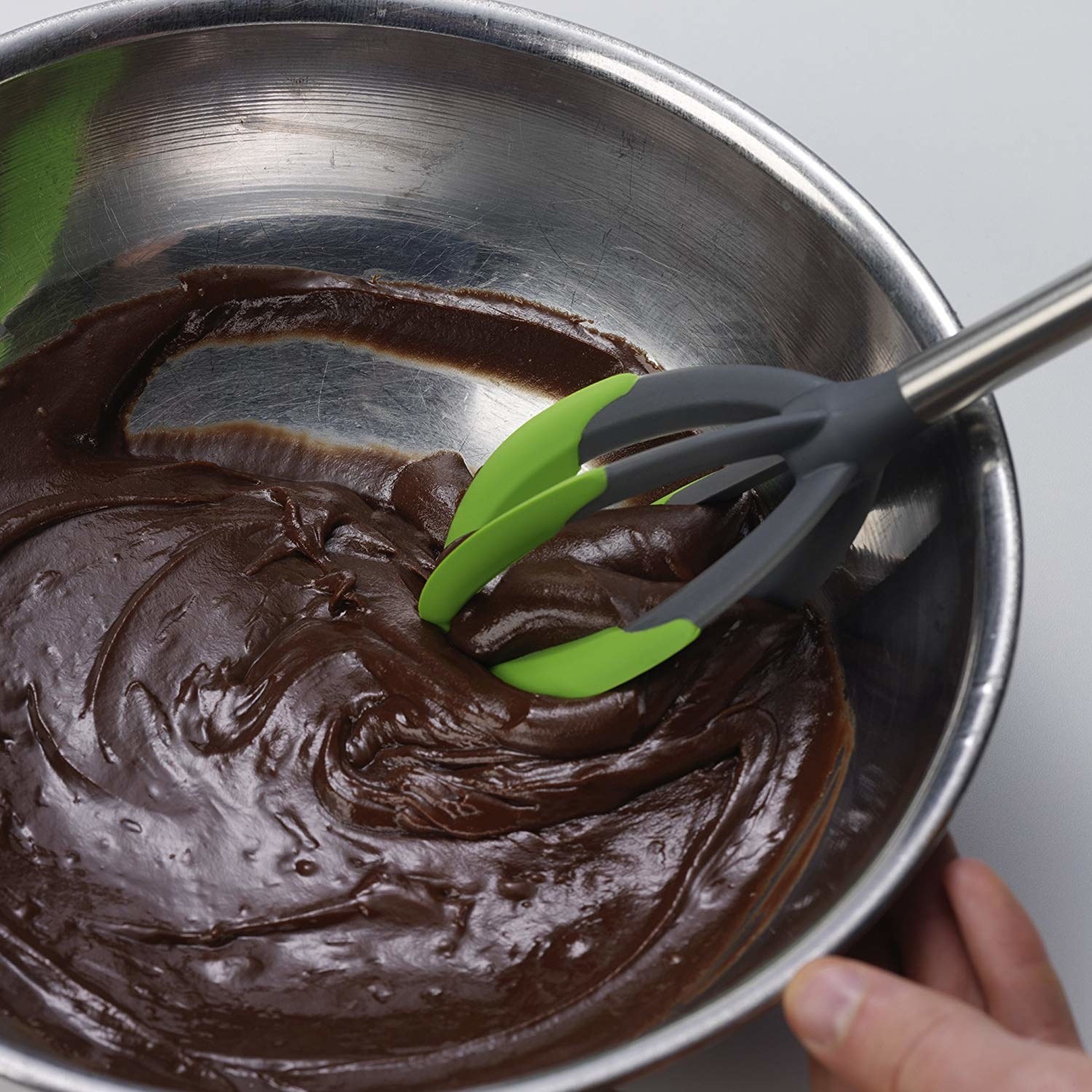 A person using a whisk-shaped silicone tool to mix chocolate batter