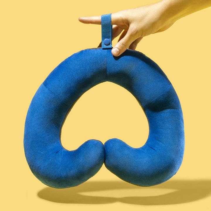 hand holds blue travel pillow with cushy curled ends that wrap around the neck