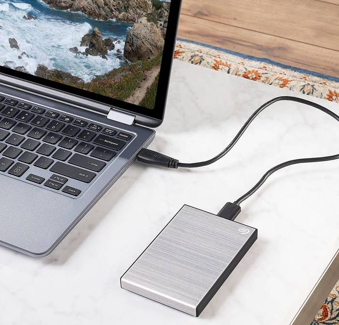 A rectangular external hard drive placed on a desk and plugged into a laptop