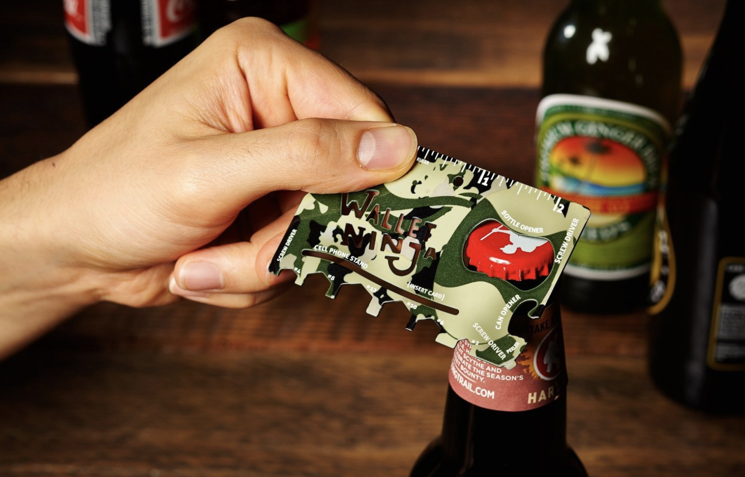 Hand uses camo print 18-in-1 multi-purpose pocket tool to open beer bottle