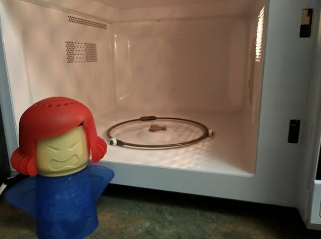 A plastic human-shaped dispenser with holes in the head next to a clean microwave 