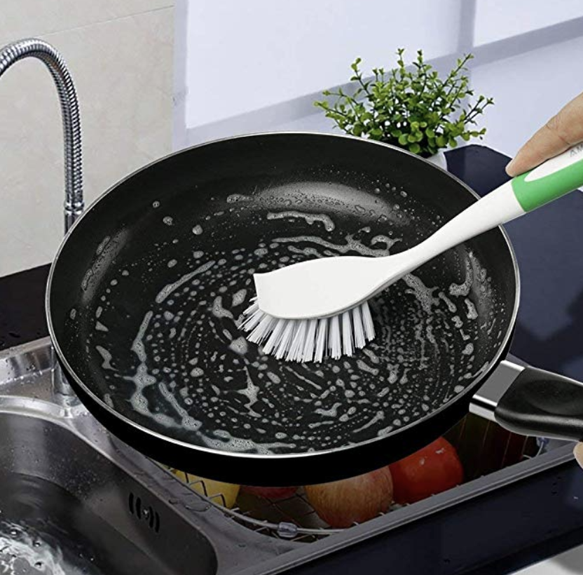 Hand holds white and green scrubber on a black pan to remove grease from it