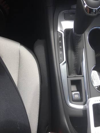 A small black seat filler wedged between the chair and console of a car 