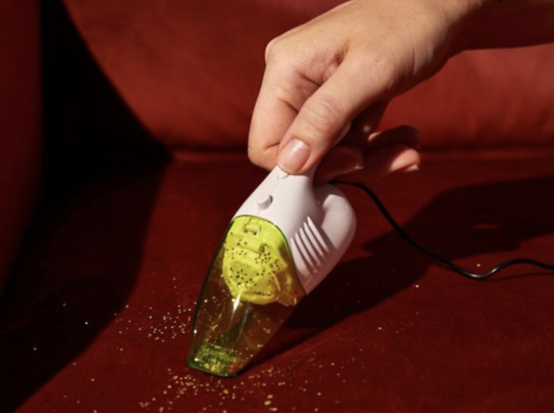 hand holds tiny yellow and white vacuum sucking up glitter from a red velvet surface
