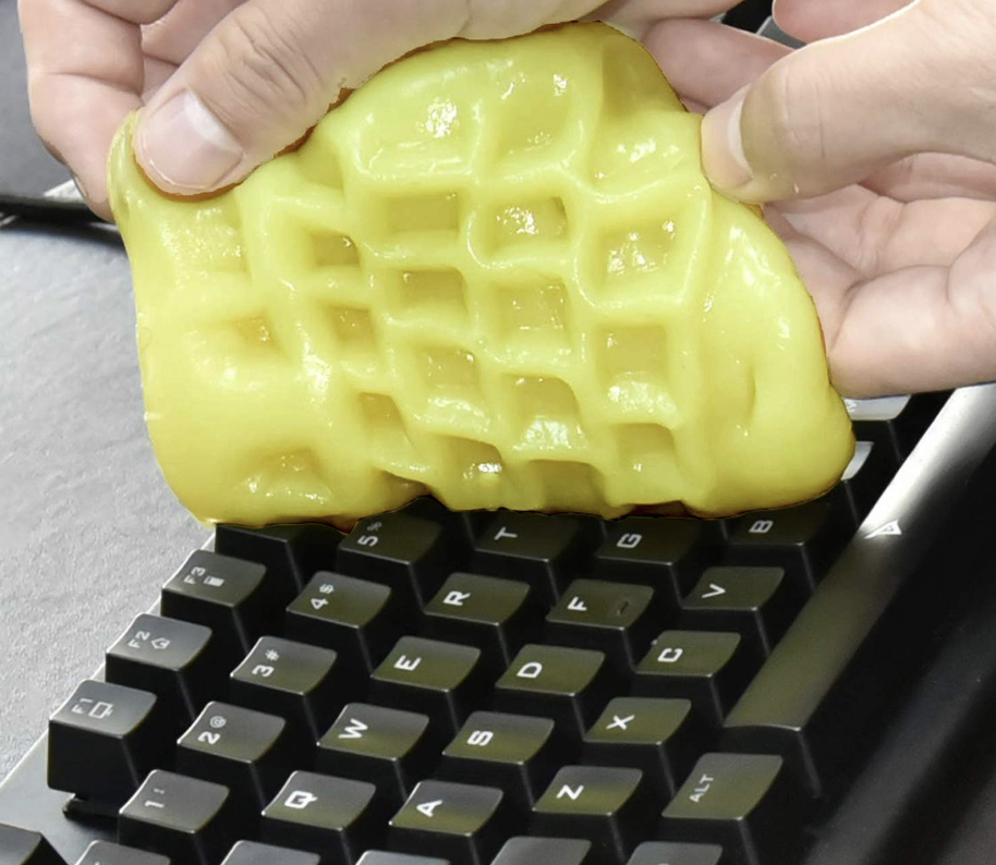 Hand lifts yellow keyboard cleaning gel away from black keyboard