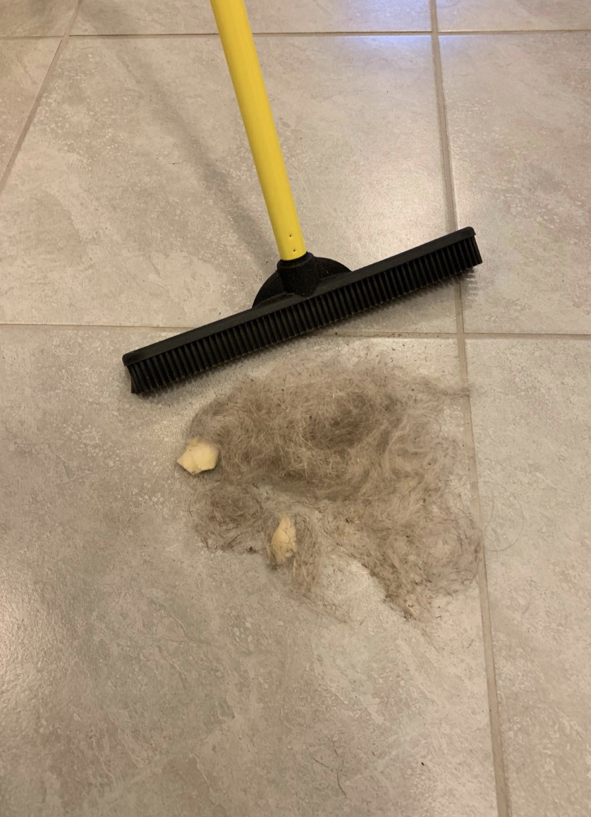 Reviewer&#x27;s black and yellow pet hair remover broom sweeps gray fur and food crumbs from kitchen tiles