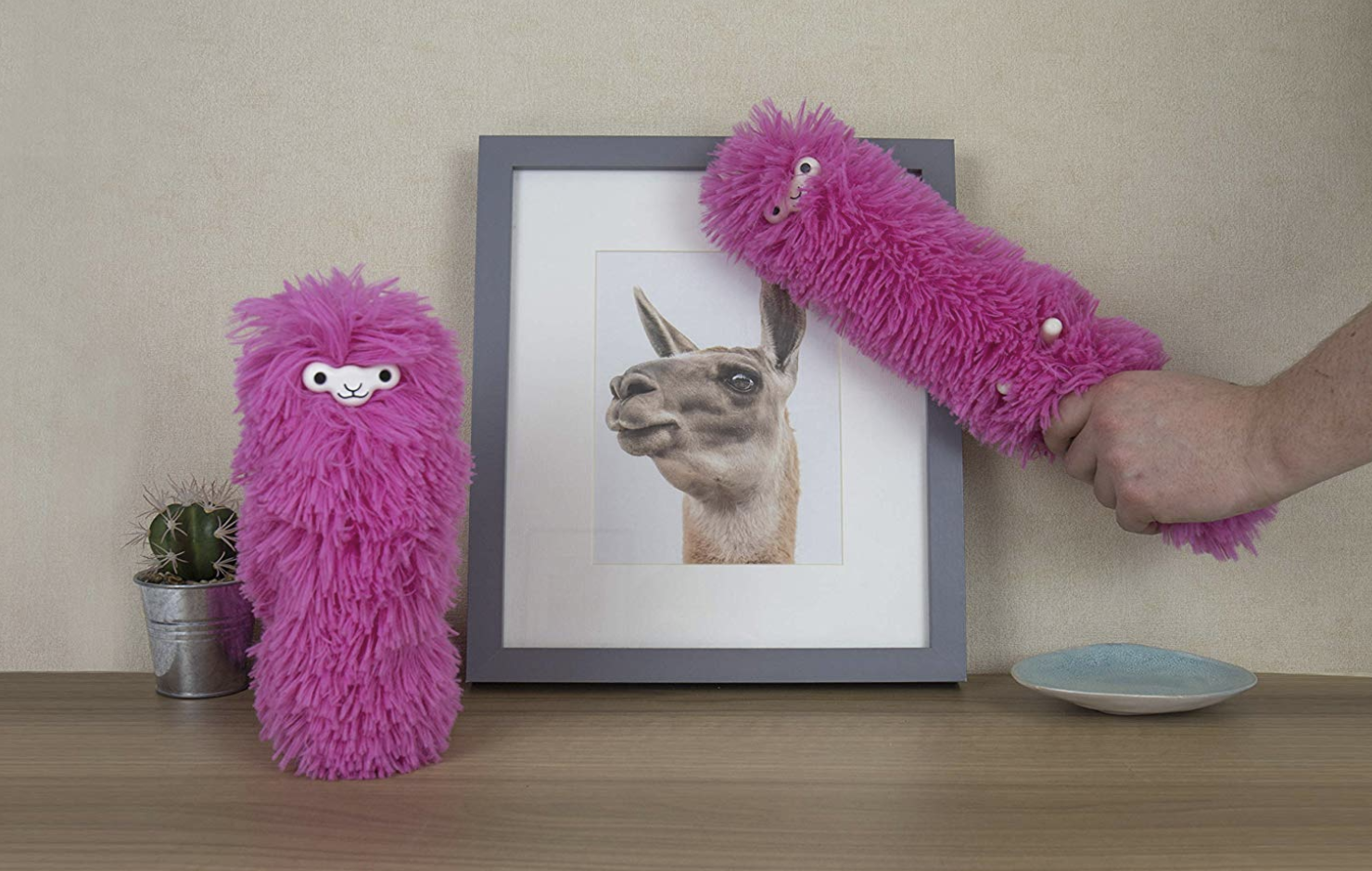 Pink llama-shaped dusters in front of llama art print on top of a table