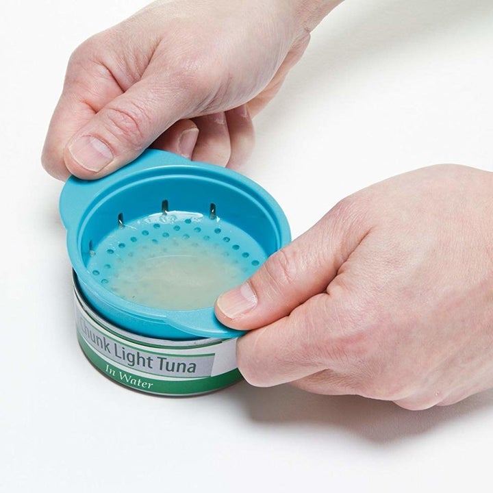 Hands using the product the other way around on a small can of tuna, pressing down to squeeze out the liquid