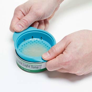 Hands using the product the other way around on a small can of tuna, pressing down to squeeze out the liquid