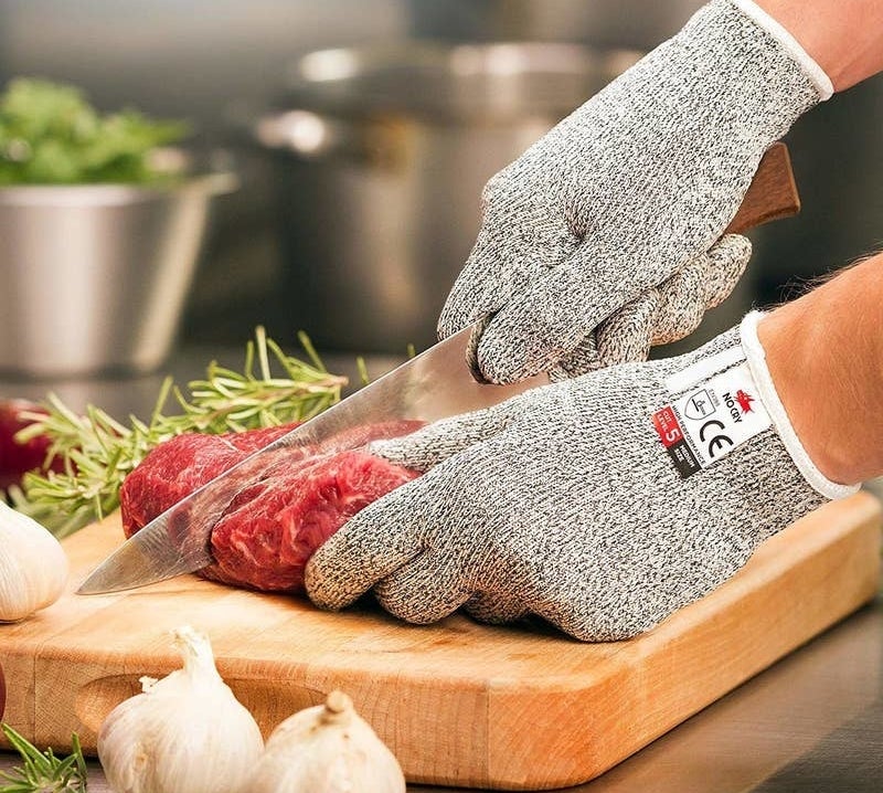 a person wearing the gray gloves while cutting a piece of raw meat