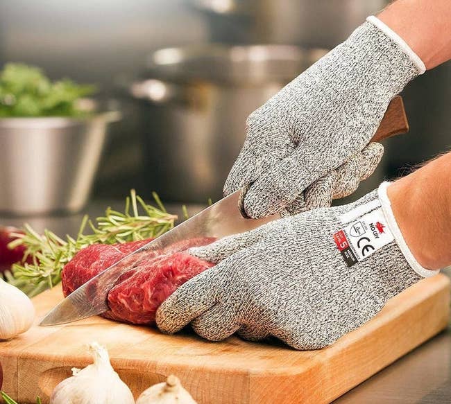a person wearing the gray gloves while cutting a piece of raw meat