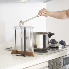 a person using the tower to keep a bag open as they ladle soup into it