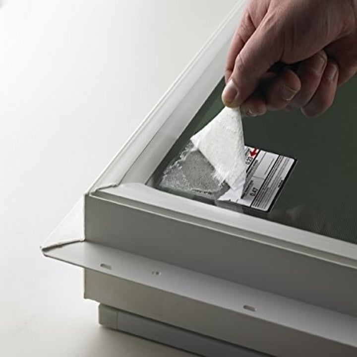 A person peeling away a sticker from a mirror, leaving behind leftover paper that can be cleaned using the spray.