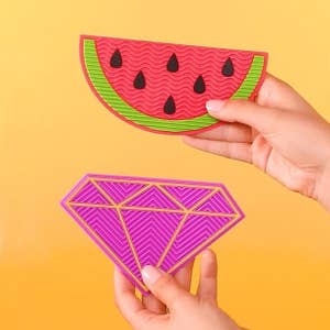 Hands holding up the palm-sized, textured mats in the watermelon and diamond shapes