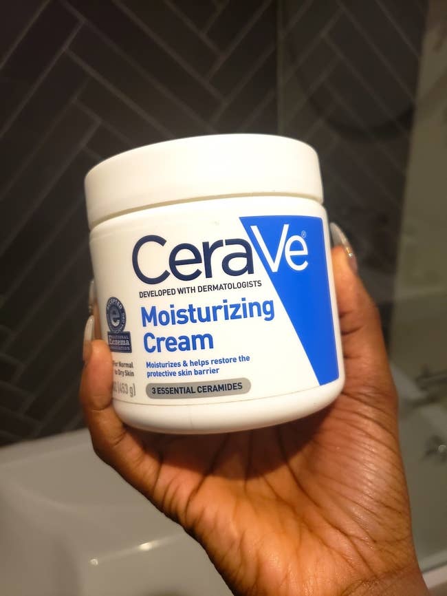 BuzzFeed writer's hand holding the tub of moisturizing cream