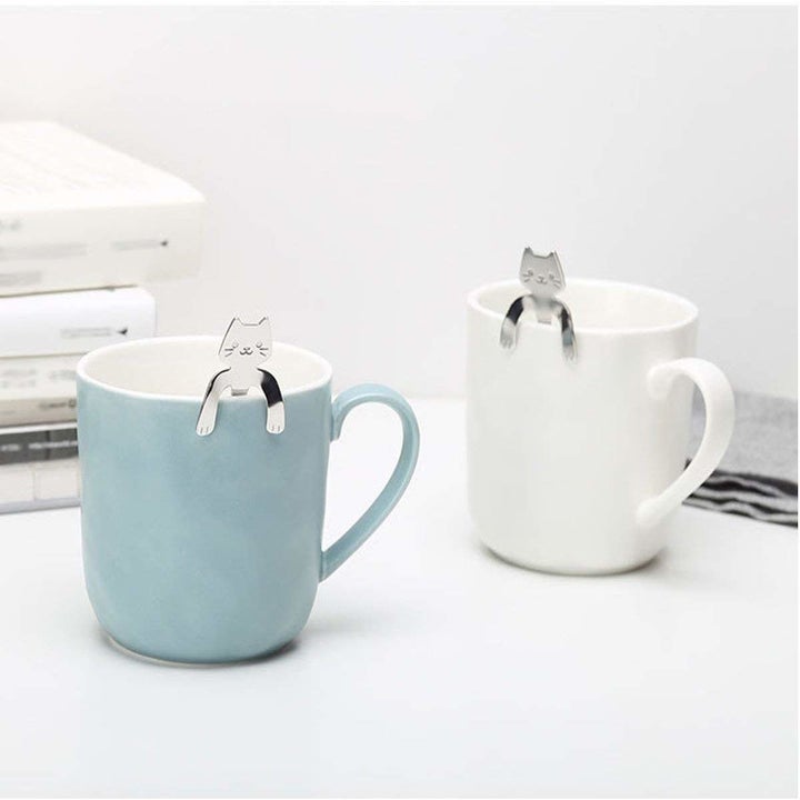 Silver cat spoons hanging on the rim of a mug by their paws 
