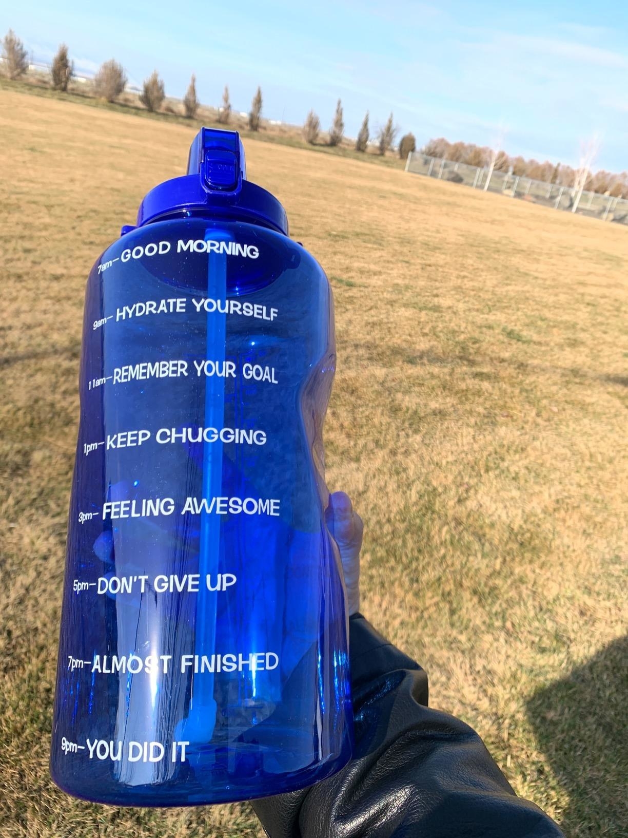 A reviewer holding a blue water bottle with motivational phrases and timestamps on the side