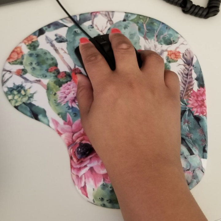 Reviewer holds onto black mouse placed on pink and green floral ergonomic mouse pad