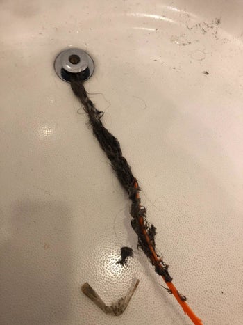 The drain snake coming out of the drain full of hair 