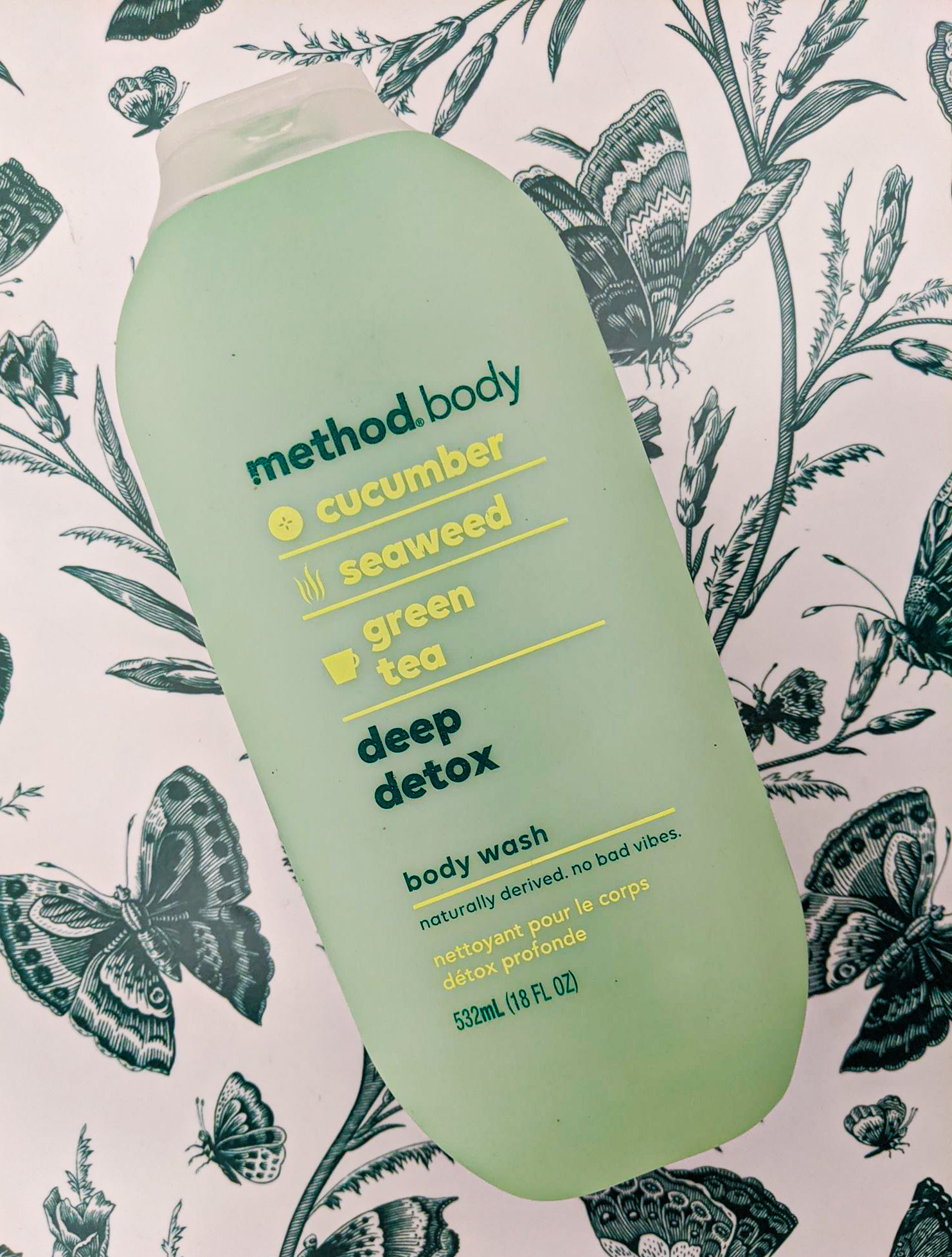 A flatlay of the bottle of body wash on a botanical-print background
