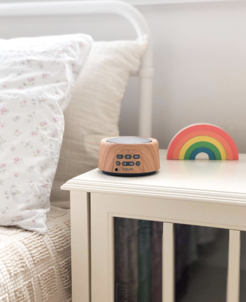 wooden white noise machine on white nightstand next to bed