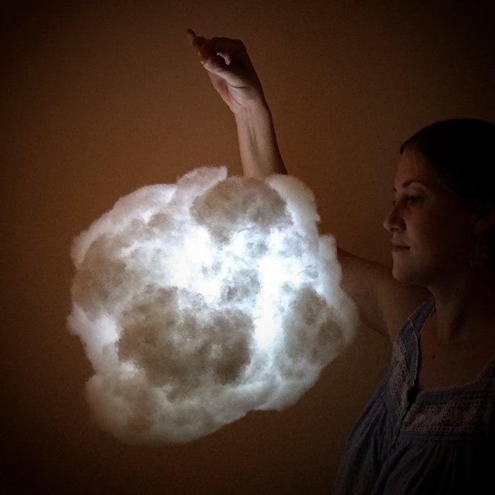 A woman hold the cloud pendant light and it has a cool -toned 
glow.