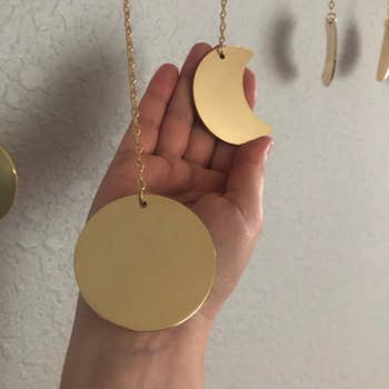 reviewer holding the charms on the moon necklace. One is a full golden moon and the other is a crescent moon.