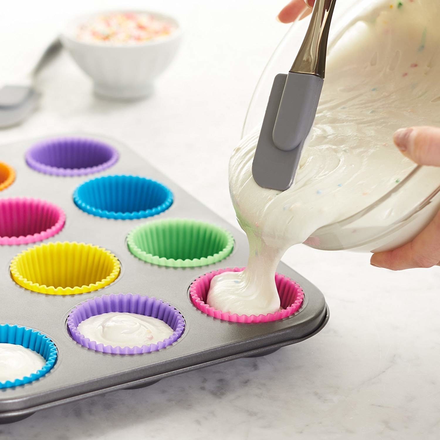 A person pouring cupcake batter into the silicone cups