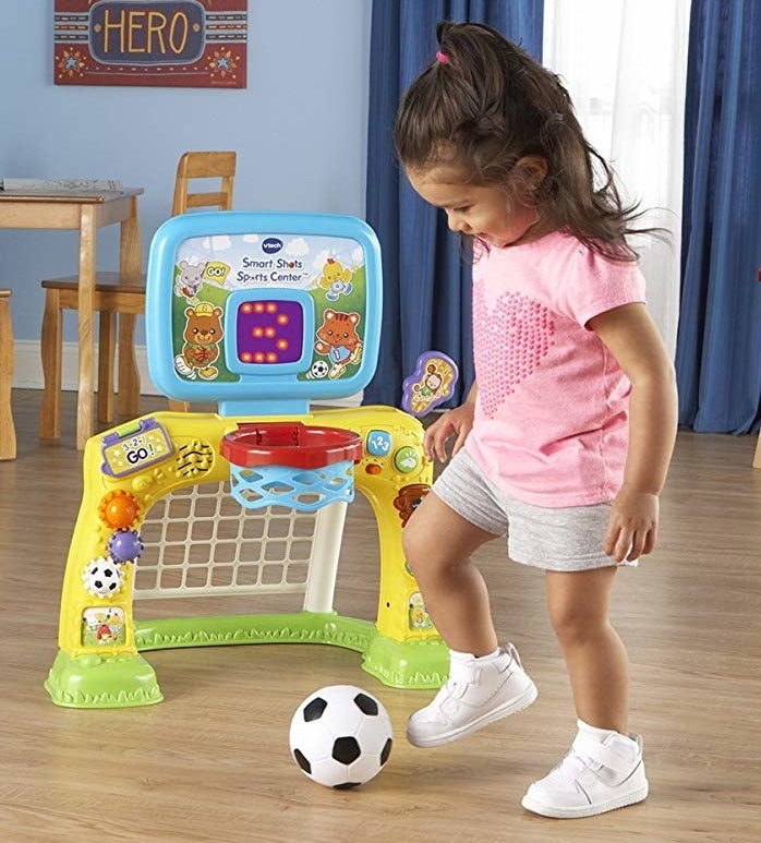 A child model playing with a small soccer ball near the colorful plastic sports center