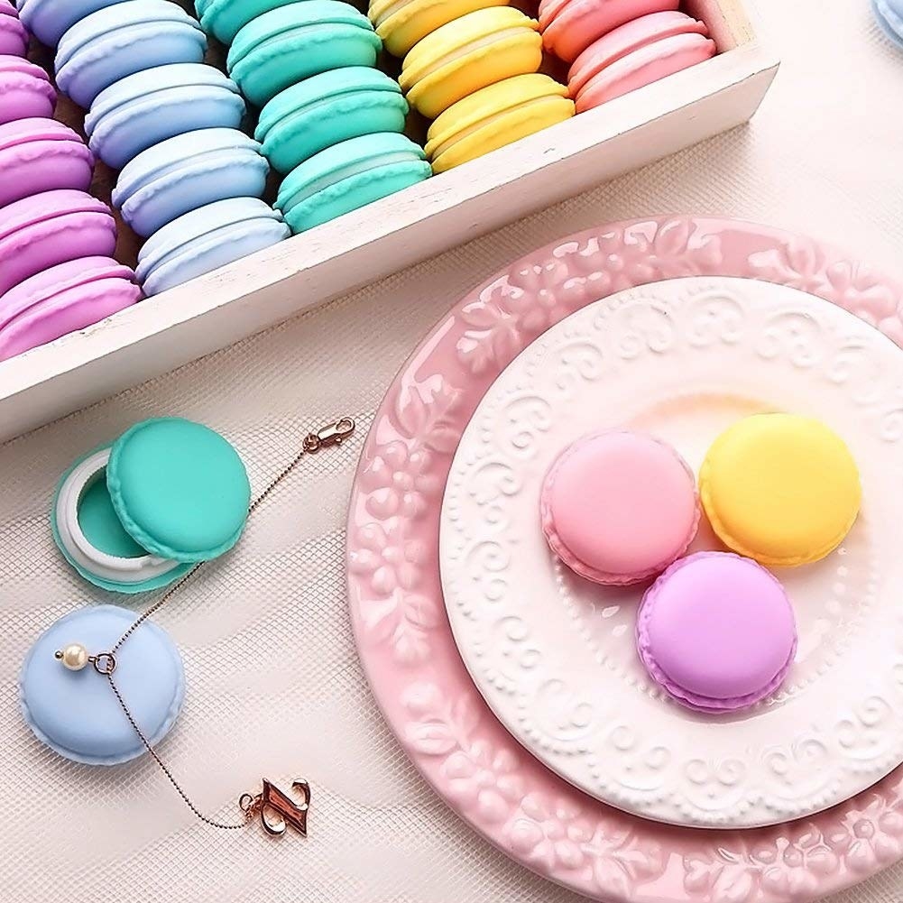 Three containers that look like macarons on a plate with two more on a cloth beside them