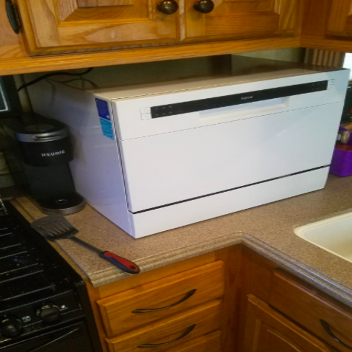 The rectangular white dishwasher sitting on a counter below a cabinet