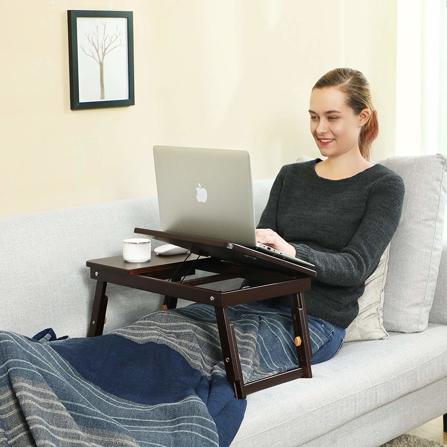 model with the brown wood desk over their lap on a couch with one half raised up, bringing a laptop higher