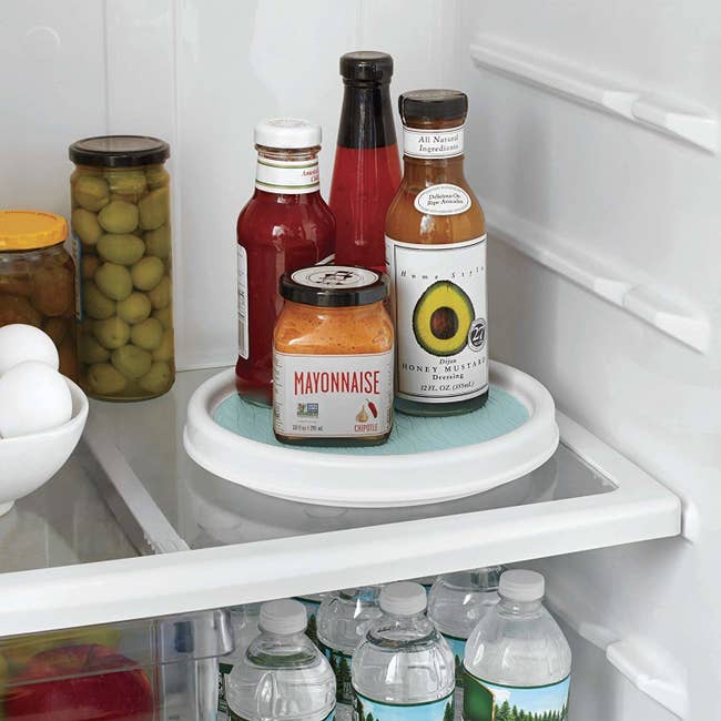 A small white turn table in a fridge with condiments on top of it 