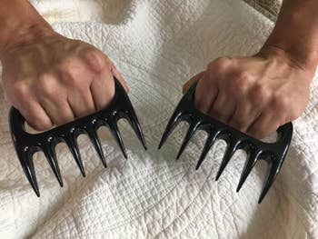 Reviewer with their fingers wrapped around the handles of two claw-like plastic shredders 
